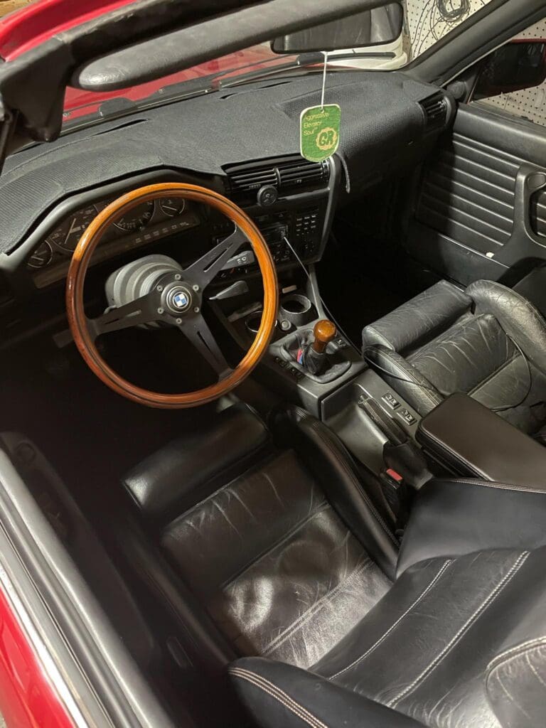 Classic car interior with wooden steering wheel and leather seats.