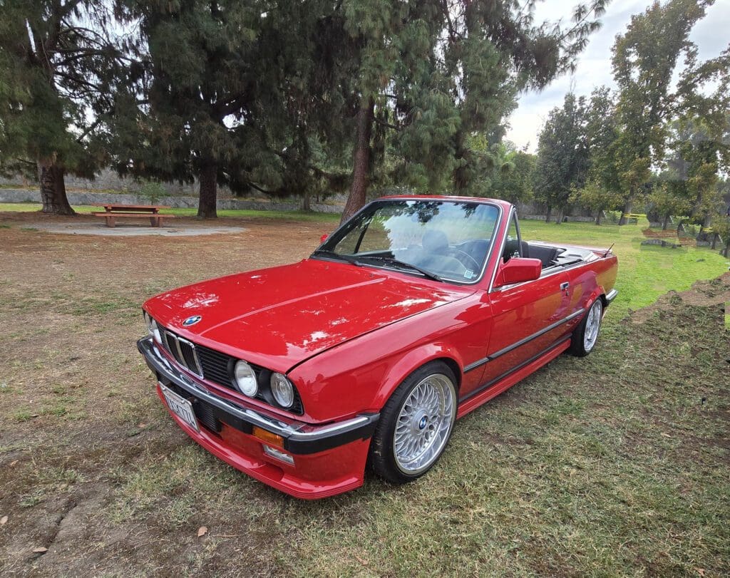 Classic red convertible parked on grass under trees.