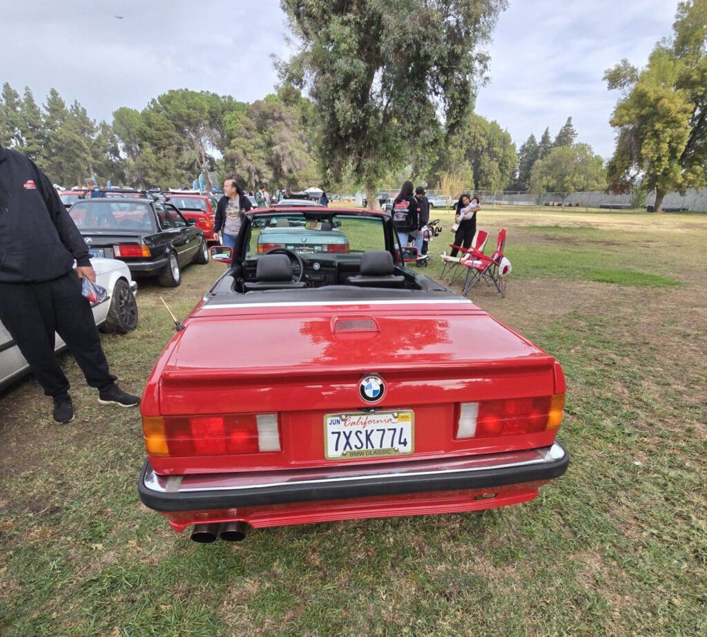 Red vintage convertible car parked on grass with people around.