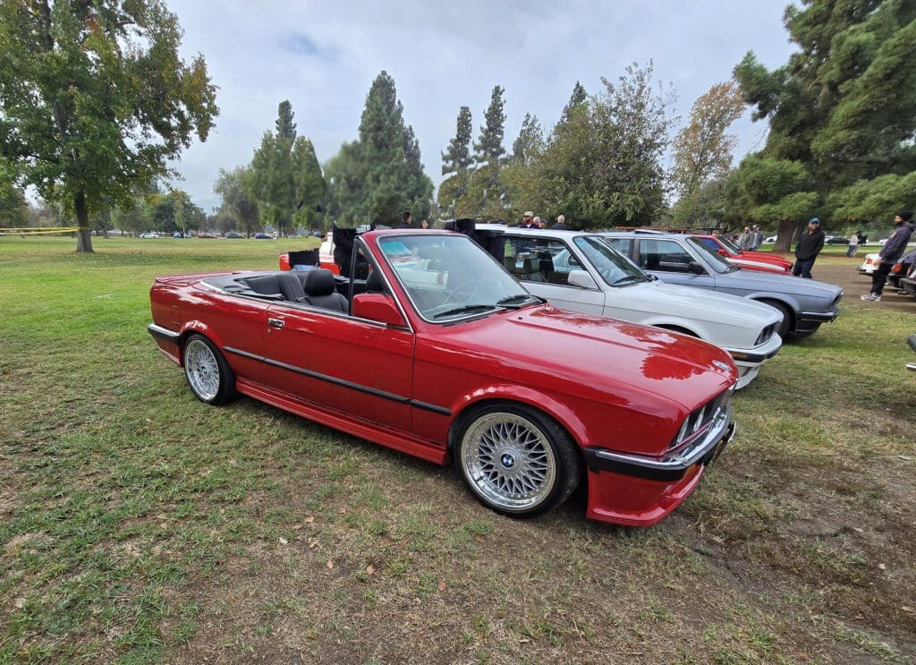 Red vintage convertible car parked on grass with other cars around.