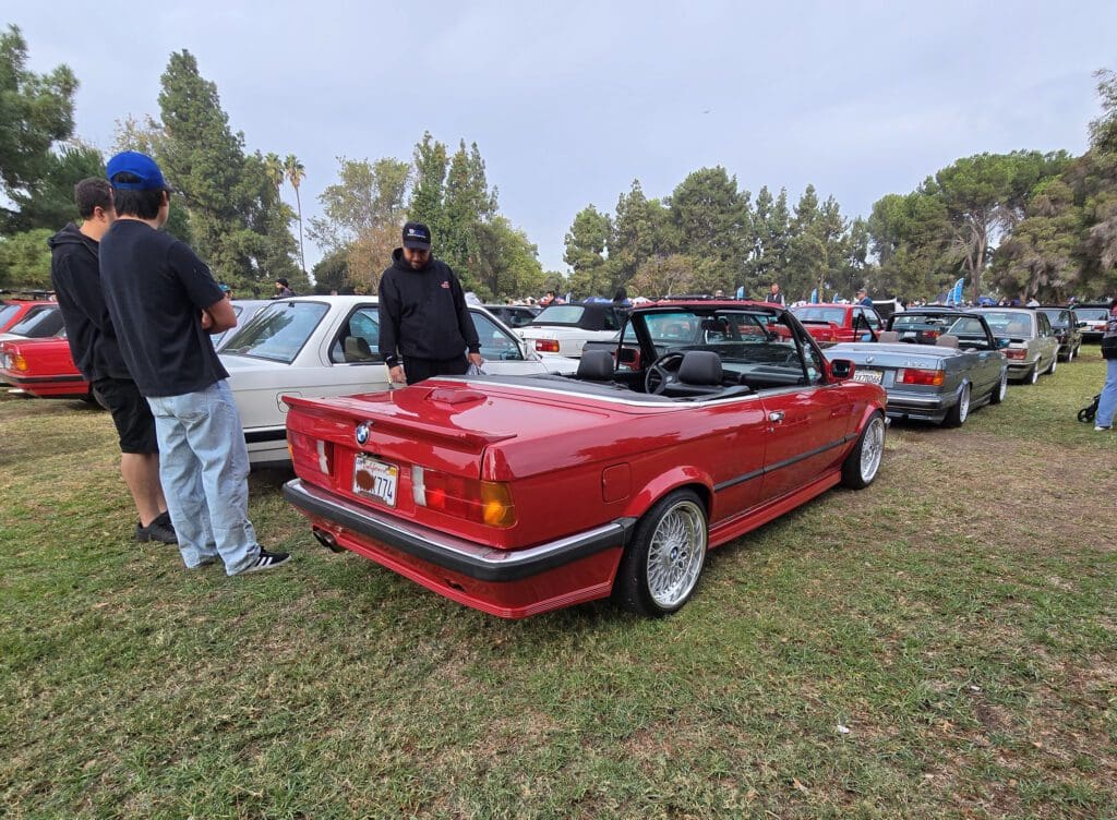 Red vintage convertible car parked on grass with other cars around.