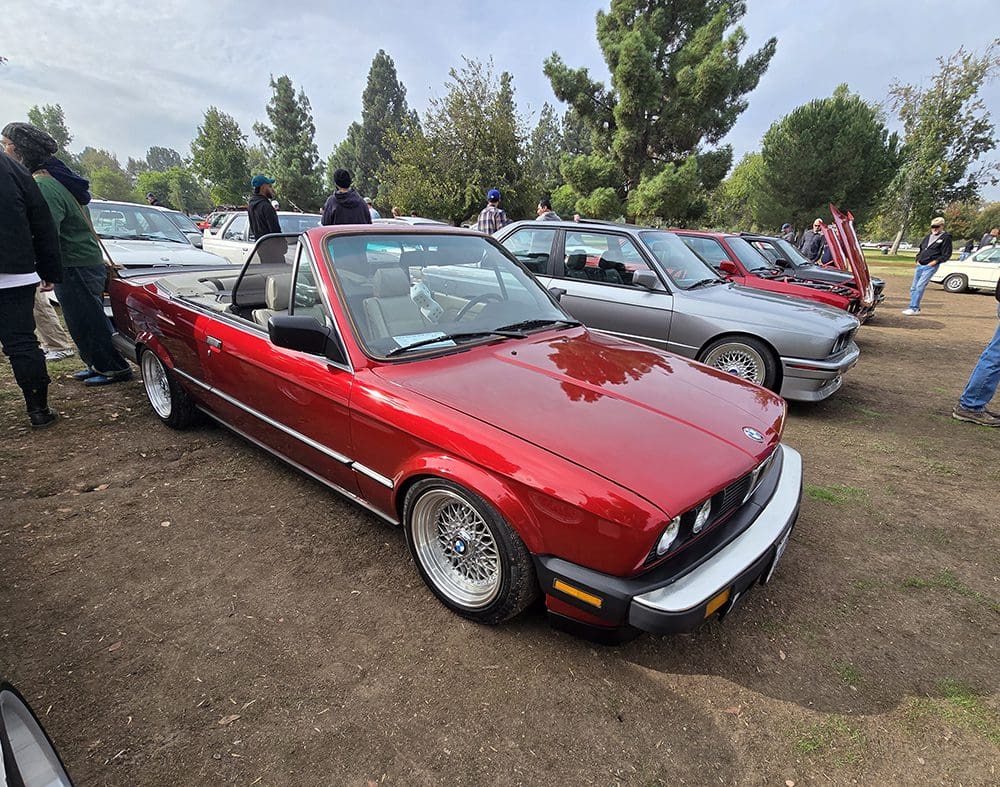 A red convertible sports car parked outdoors with other cars.