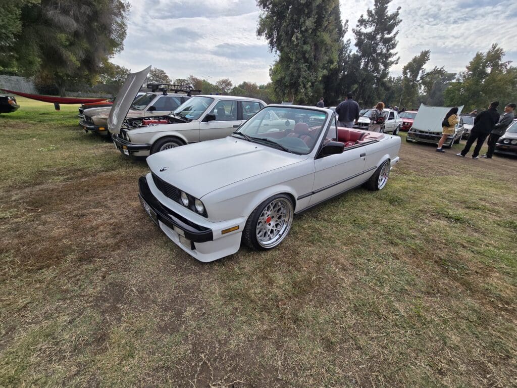 White convertible car parked on grass at a car event.