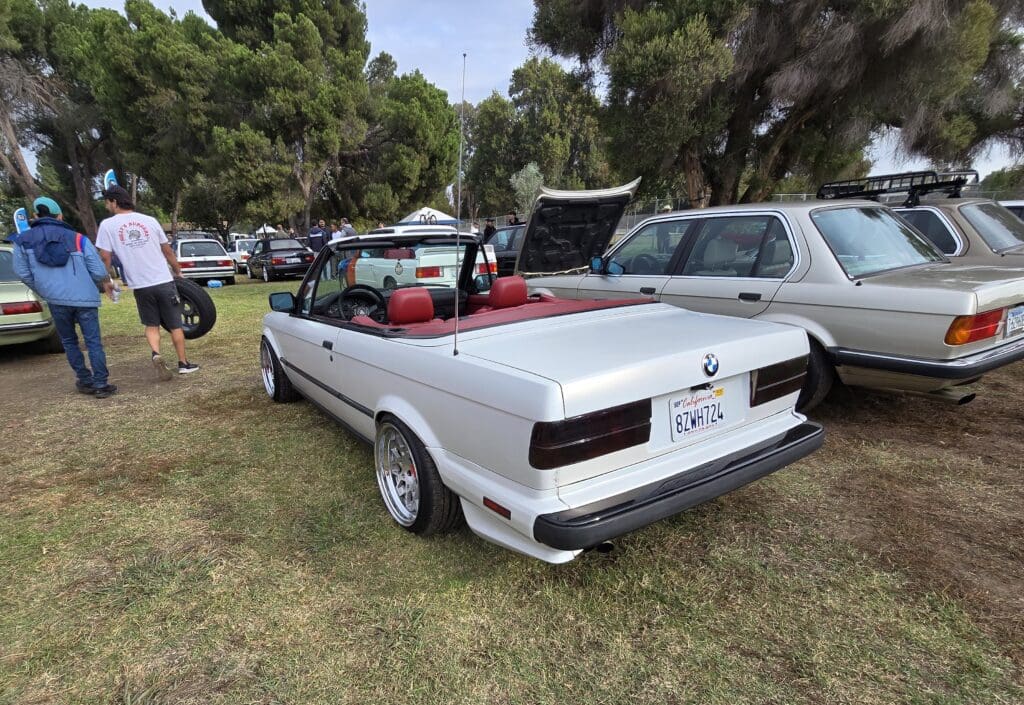 White convertible car parked on grass with trees in background.