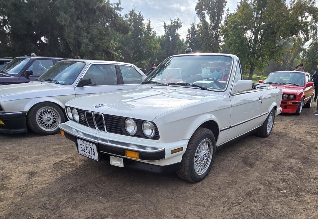 Classic white convertible car parked outdoors with trees in the background.