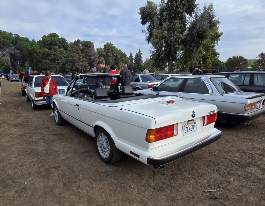 White vintage convertible car parked outdoors among other vehicles.