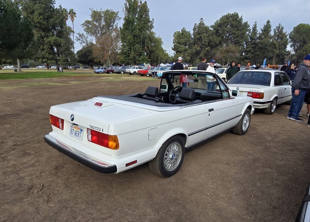 White vintage convertible car parked outdoors on grass.