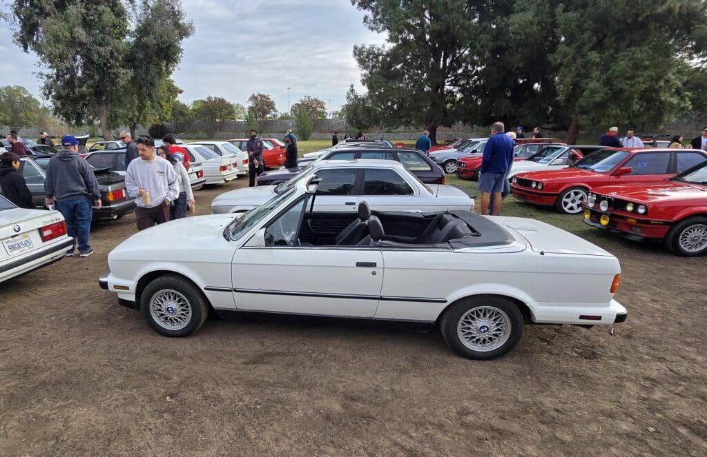 White classic convertible car parked among other vehicles at an outdoor event.