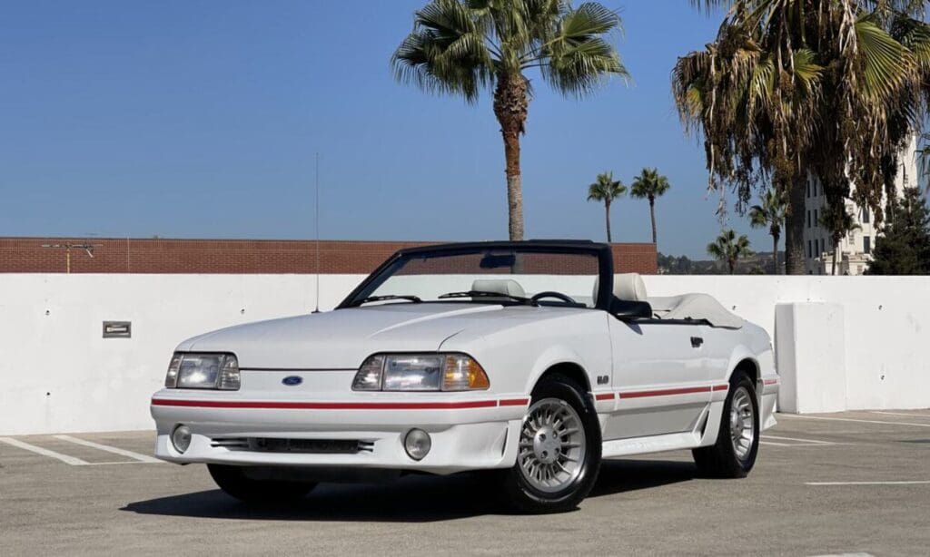 White convertible Ford Mustang parked under palm trees on a sunny day.