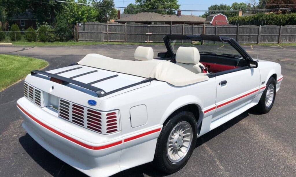 White convertible Ford Mustang parked under palm trees on a sunny day.