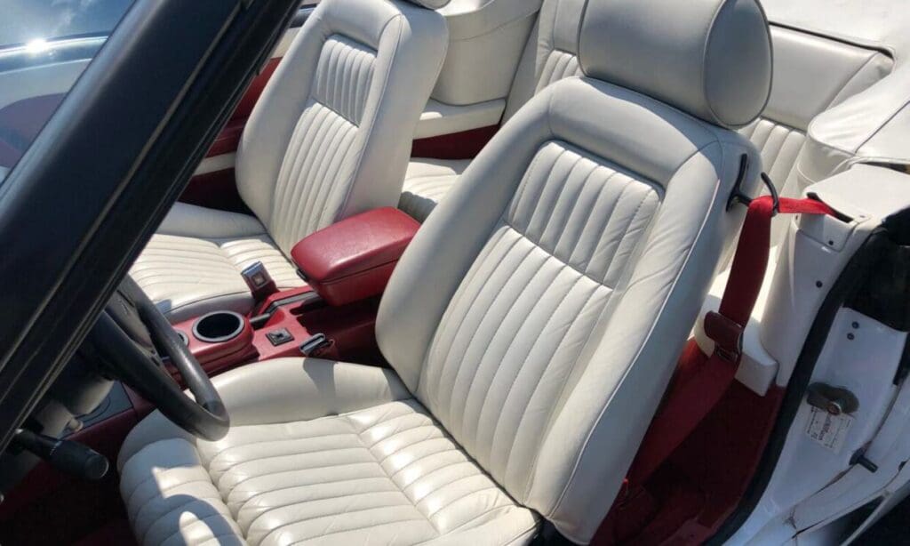 Close-up of white leather car seats with a red center console.
