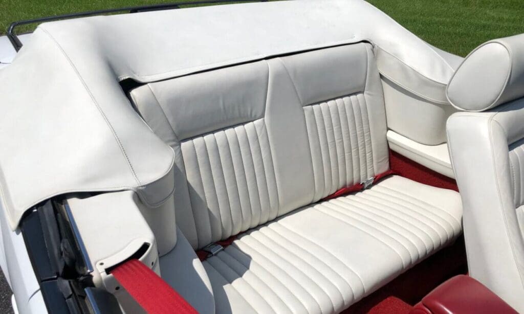 White leather car backseat with vertical stitching and red accents.