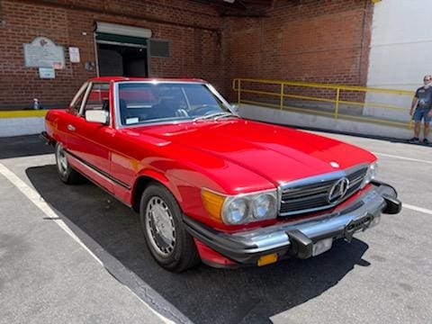 Classic red Mercedes-Benz convertible parked in a sunlit urban area.