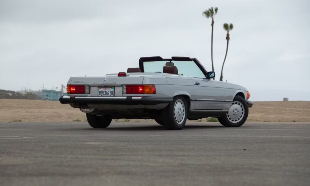 Classic white convertible car parked near palm trees on a cloudy day.