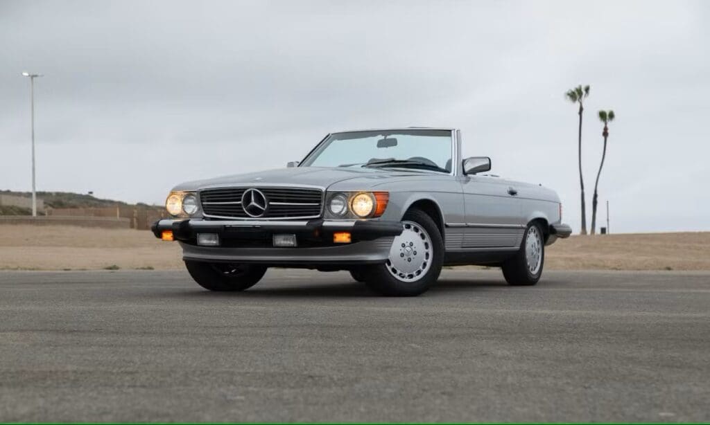 Classic silver Mercedes convertible parked on asphalt under cloudy sky.