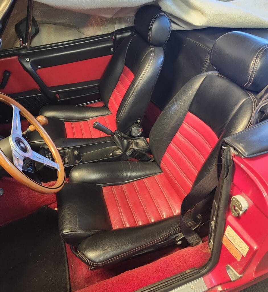 Vintage car interior with black and red leather seats and wooden steering wheel.