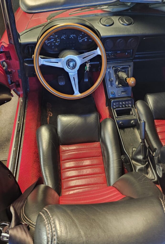 Classic car interior with red leather seats and a wooden steering wheel.