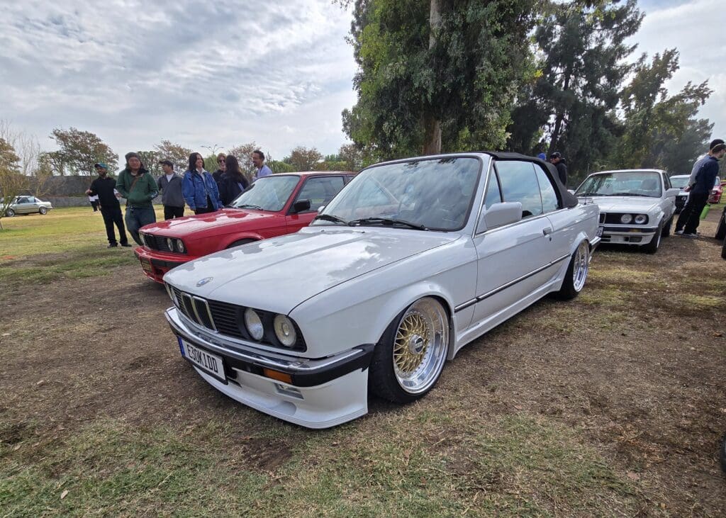 Classic white BMW E30 with gold rims at a car meet.