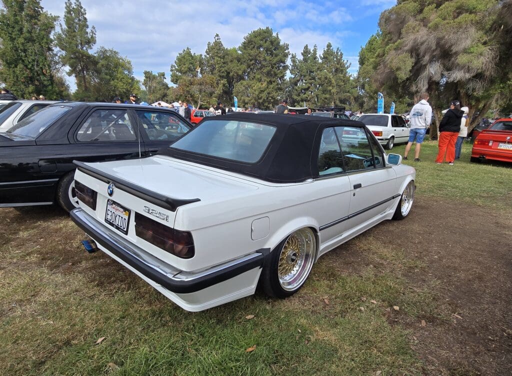 White convertible car parked on grass with people in the background.