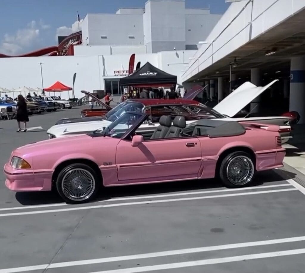 A pink convertible car parked outdoors near a building.