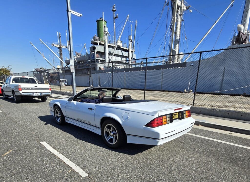 White convertible sports car parked near a large ship.
