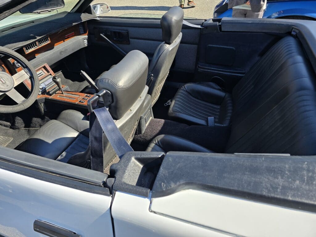 Interior of a vintage convertible car with beige seats and a wooden steering wheel.