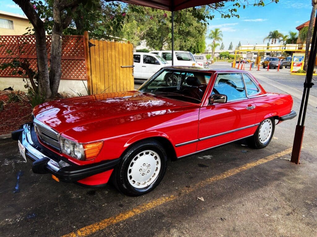 Classic red vintage car parked under a tree on a sunny day.