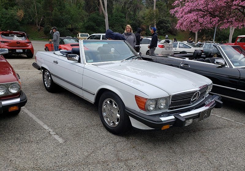 Classic white convertible car parked outdoors with people nearby.