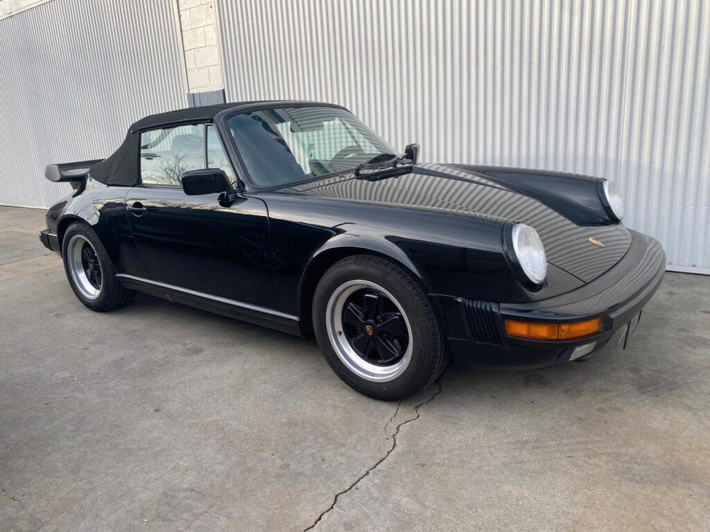 Black classic Porsche convertible parked outdoors on concrete.