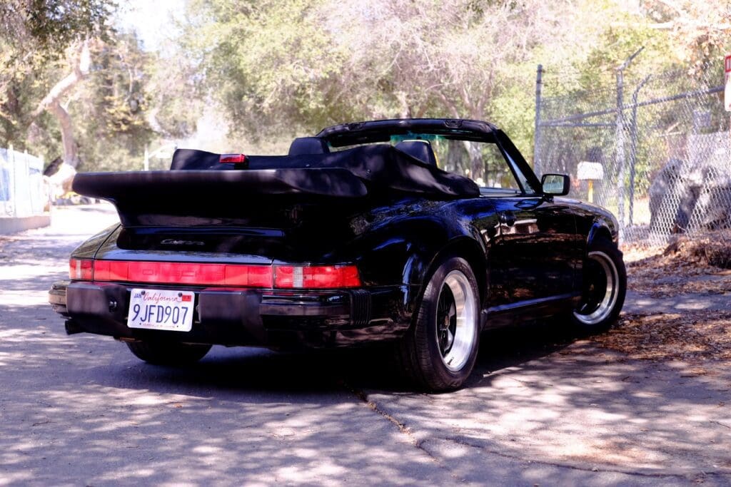 Black classic Porsche convertible parked outdoors on concrete.