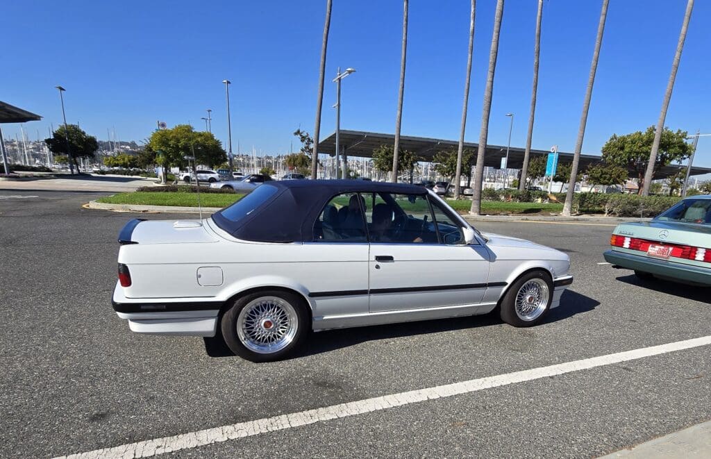 White classic convertible car parked by the curb on a sunny day.