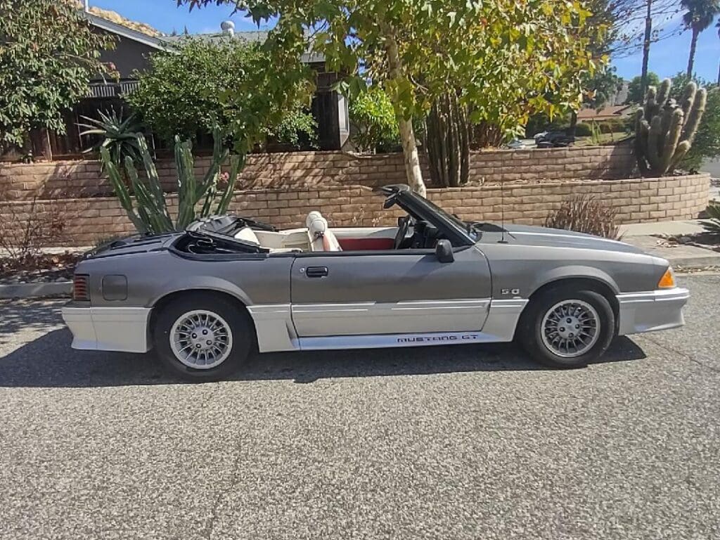 A silver convertible car parked on the street under trees.