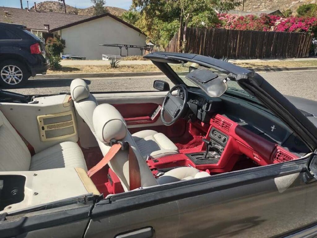 Classic convertible car interior with red and white leather seats under sunlight.