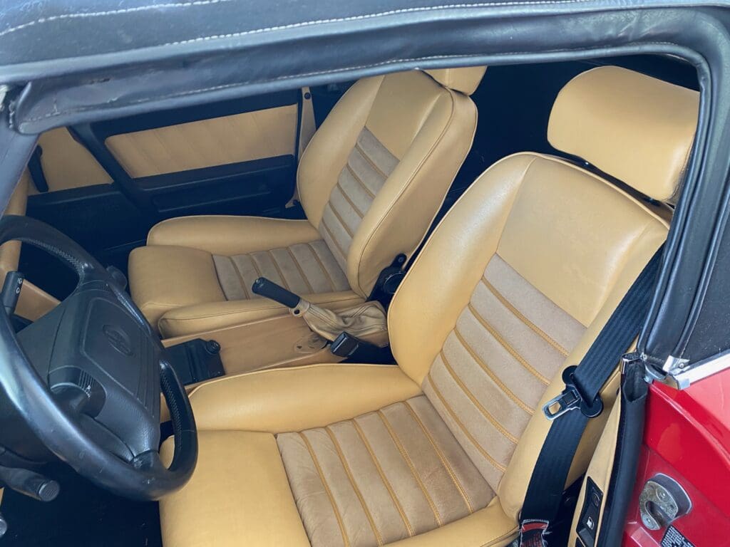 Vintage car interior with tan leather seats and manual gear shift.