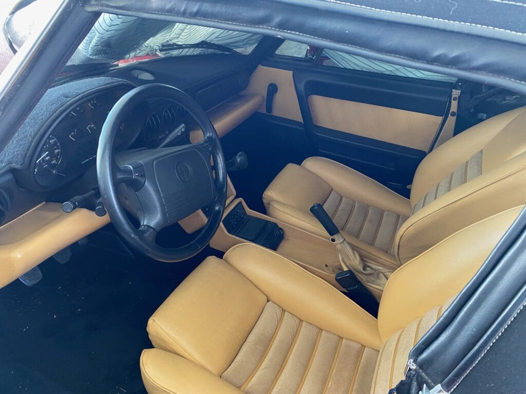 Interior of a vintage car with tan leather seats and a classic steering wheel.