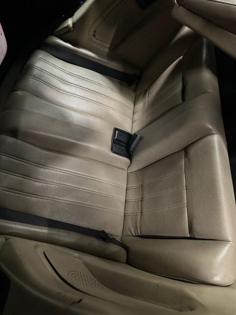 Rear seat of a car with beige upholstery and seatbelt.