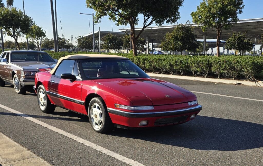 A red classic car parked in a sunny outdoor lot.