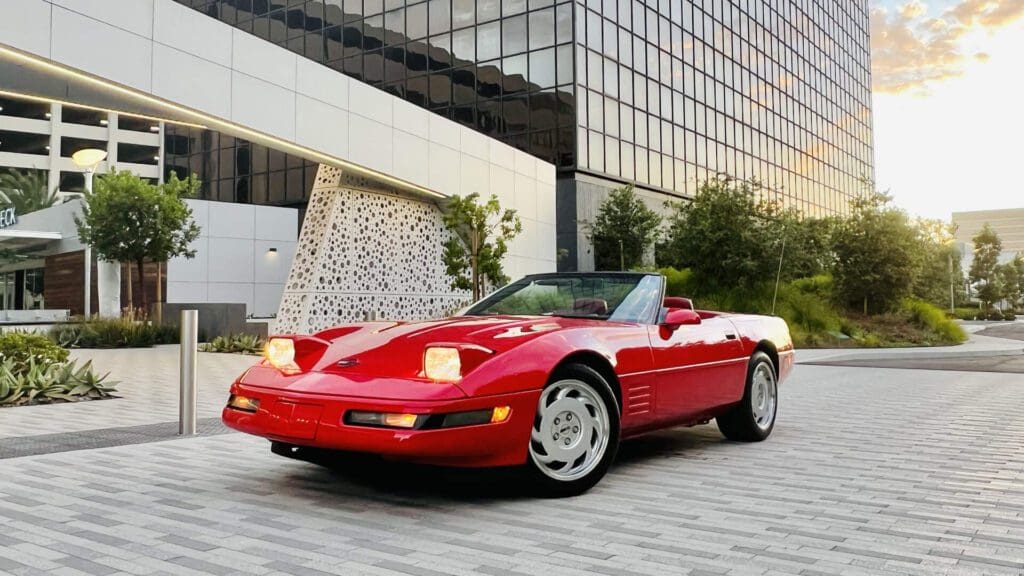 Red convertible sports car parked on a city street at sunset.