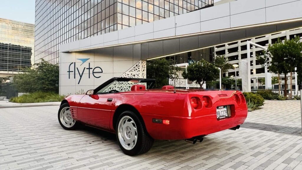 Red convertible sports car parked on a city street at sunset.