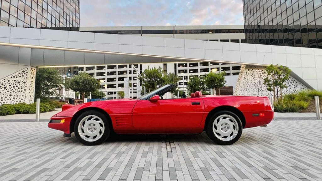 Red convertible sports car parked outdoors with a cityscape background.