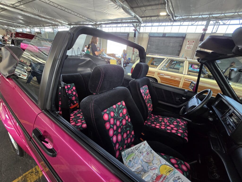 A pink convertible car parked in a sunny outdoor area.