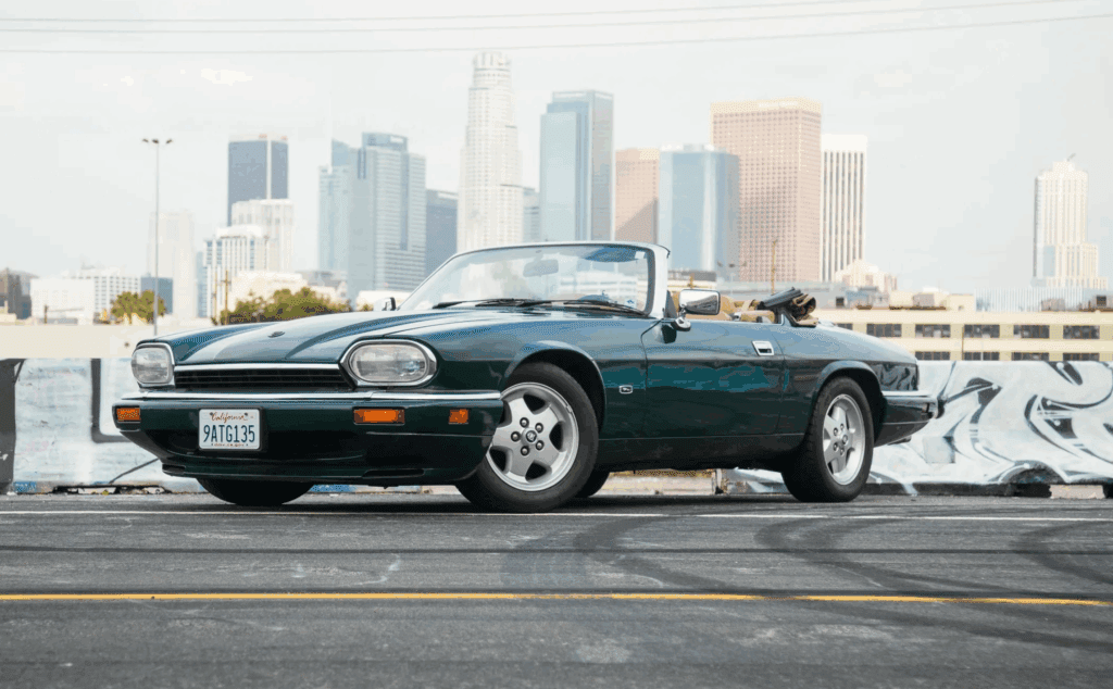Classic green convertible car parked with city skyline in background.