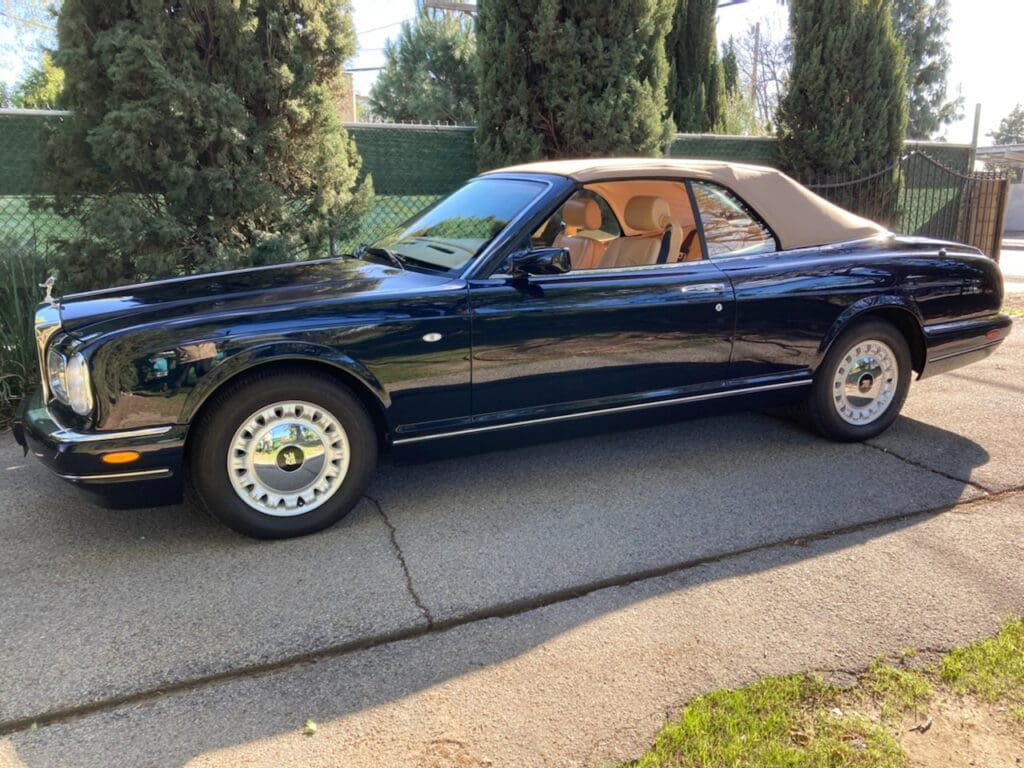 Classic black convertible car parked on a driveway beside trees.