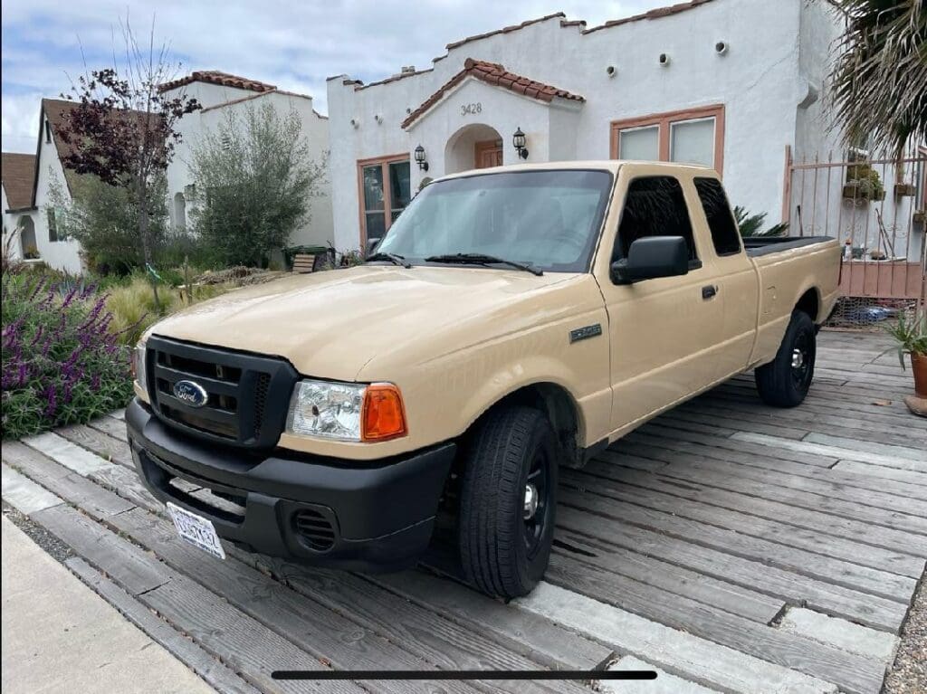Beige Ford Ranger parked in front of a rustic house.