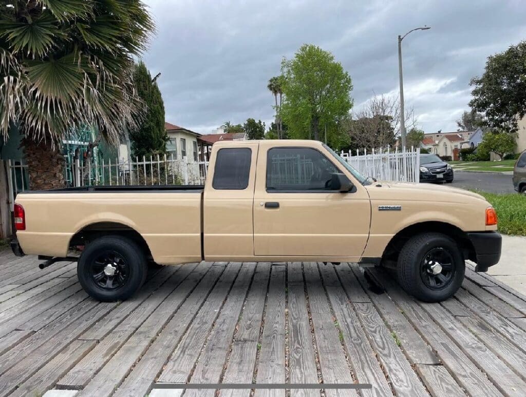 Beige pickup truck parked on wooden planks near houses.