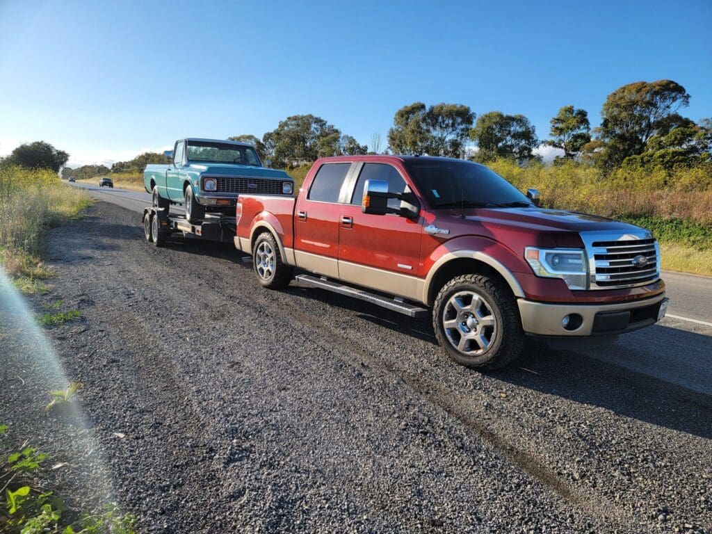 A red pickup truck towing a trailer on a gravel road under a clear blue sky.