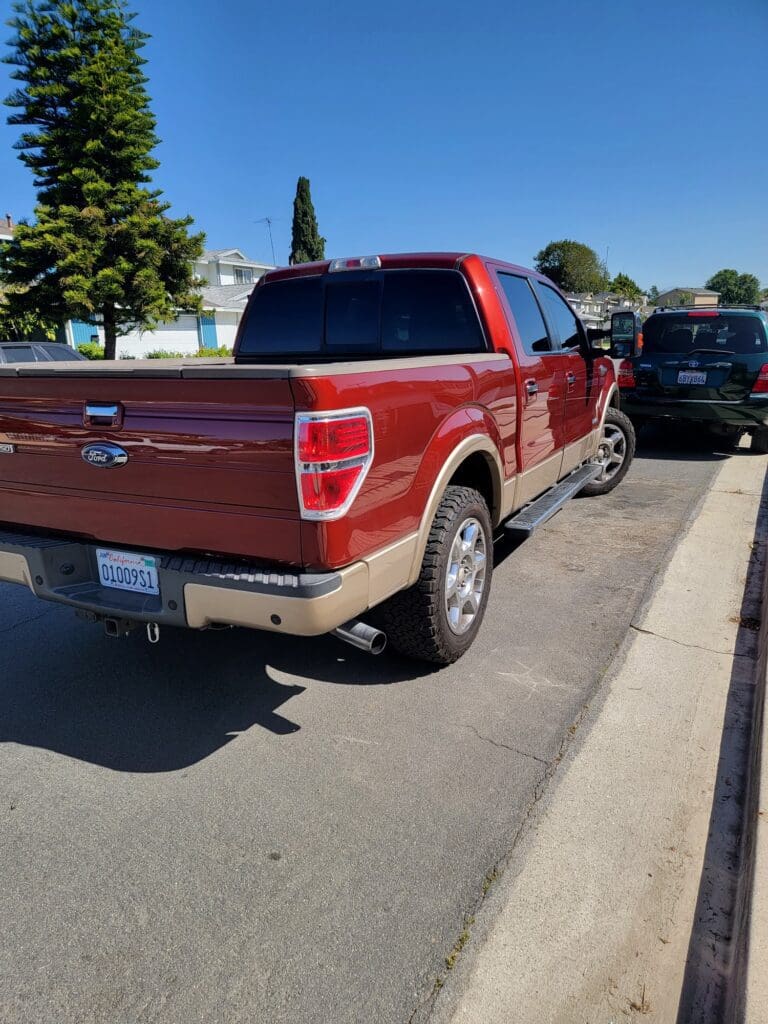 Red pickup truck parked on a sunny street near a curb.