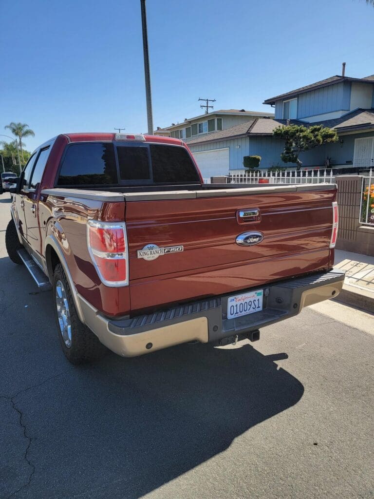 Red Ford F-150 pickup truck parked in a sunny residential area.
