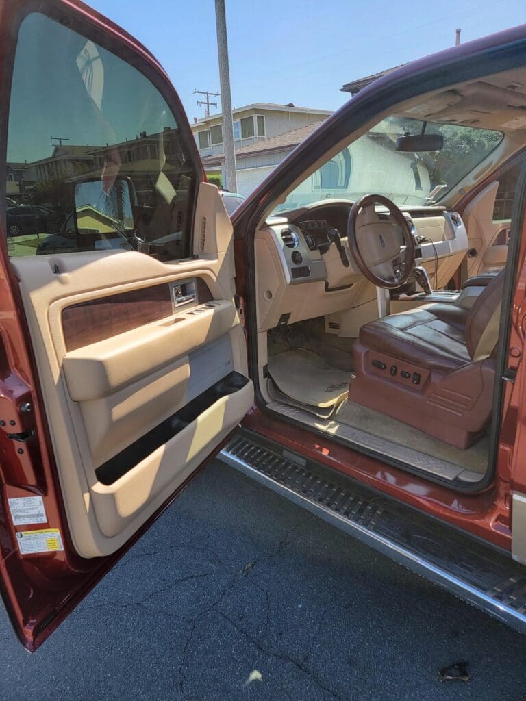 Open car door showing the interior of a red vehicle with a clear view of the driver's seat and dashboard.