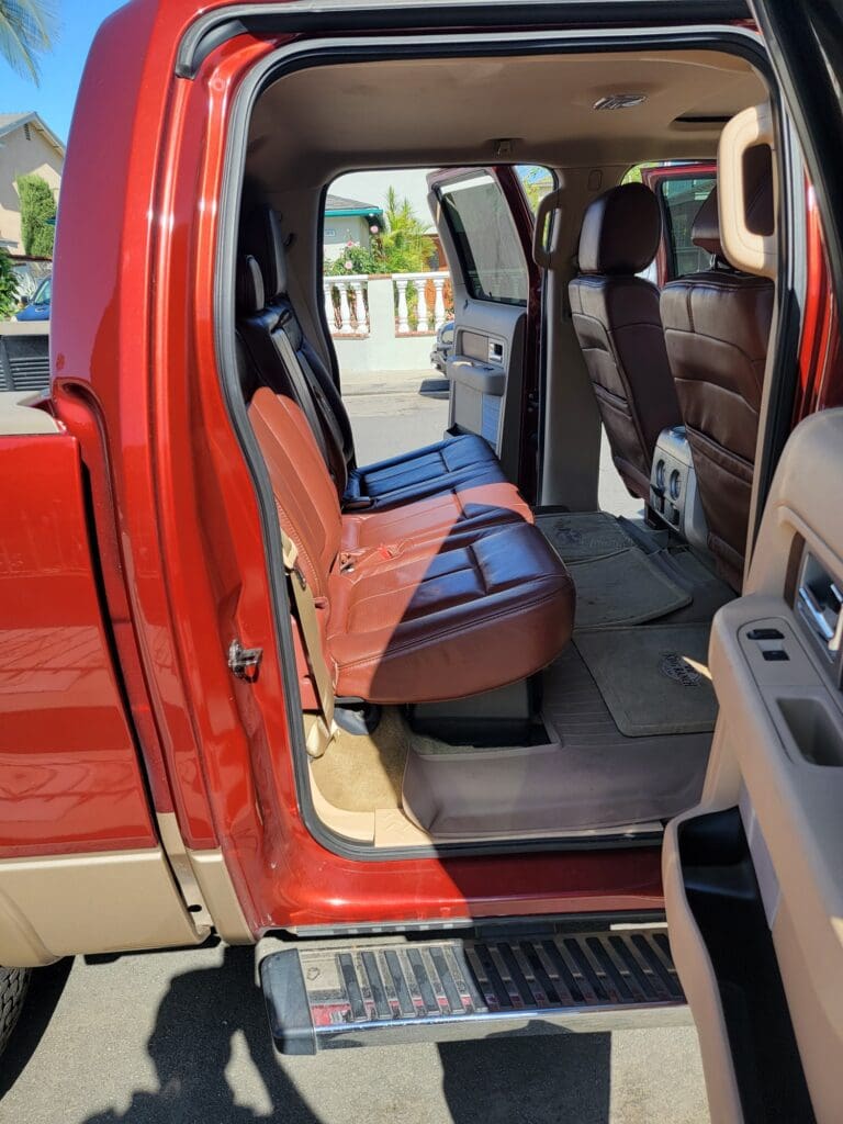 Open door view of a red truck's spacious rear interior with black and brown seats.